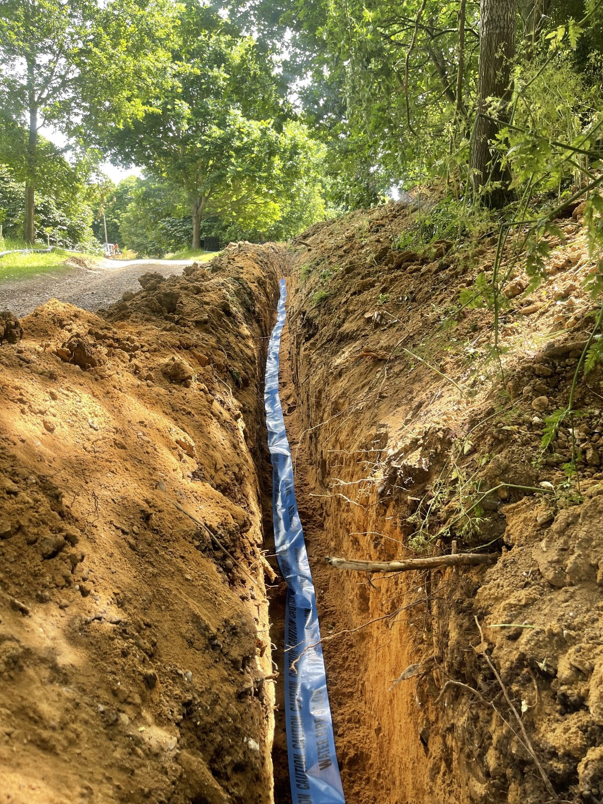 Underground water main installation in Norfolk with new blue mains pipe laid in a trench