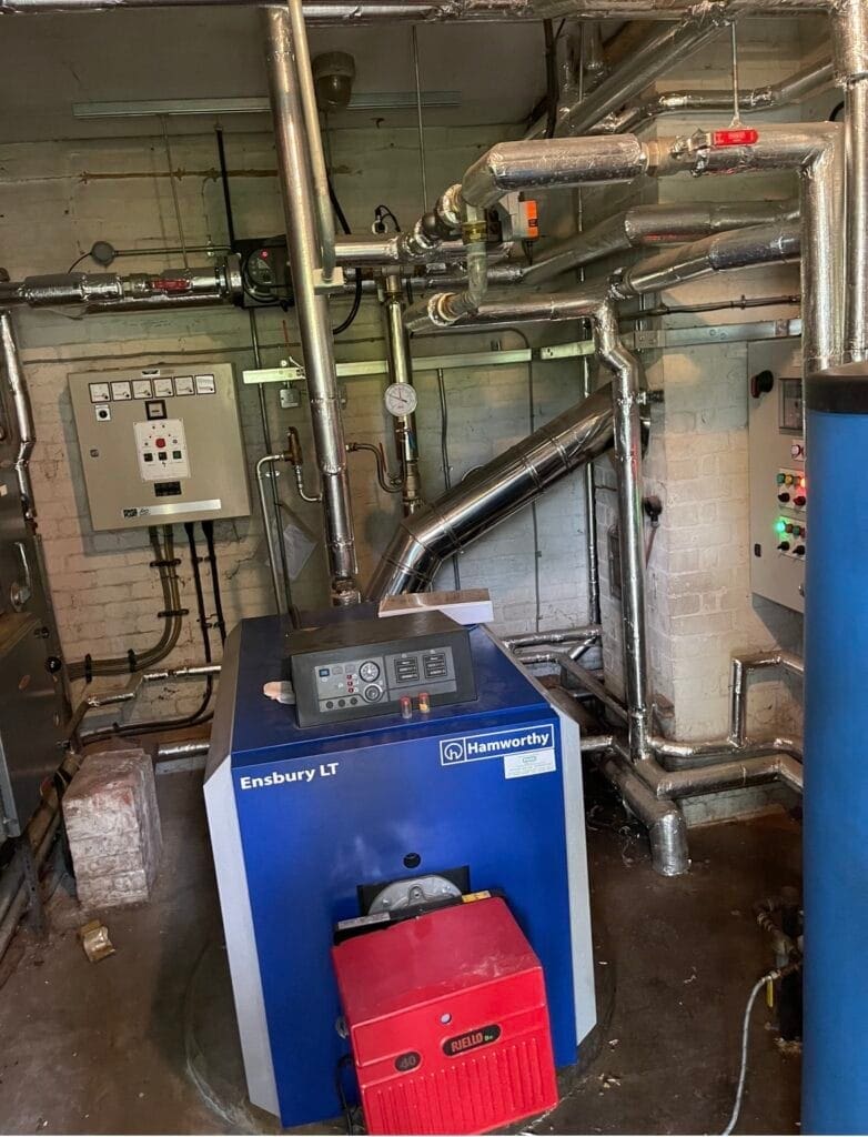 Commercial boiler plant room with large boiler, flue system and heating pipework for servicing and maintenance
